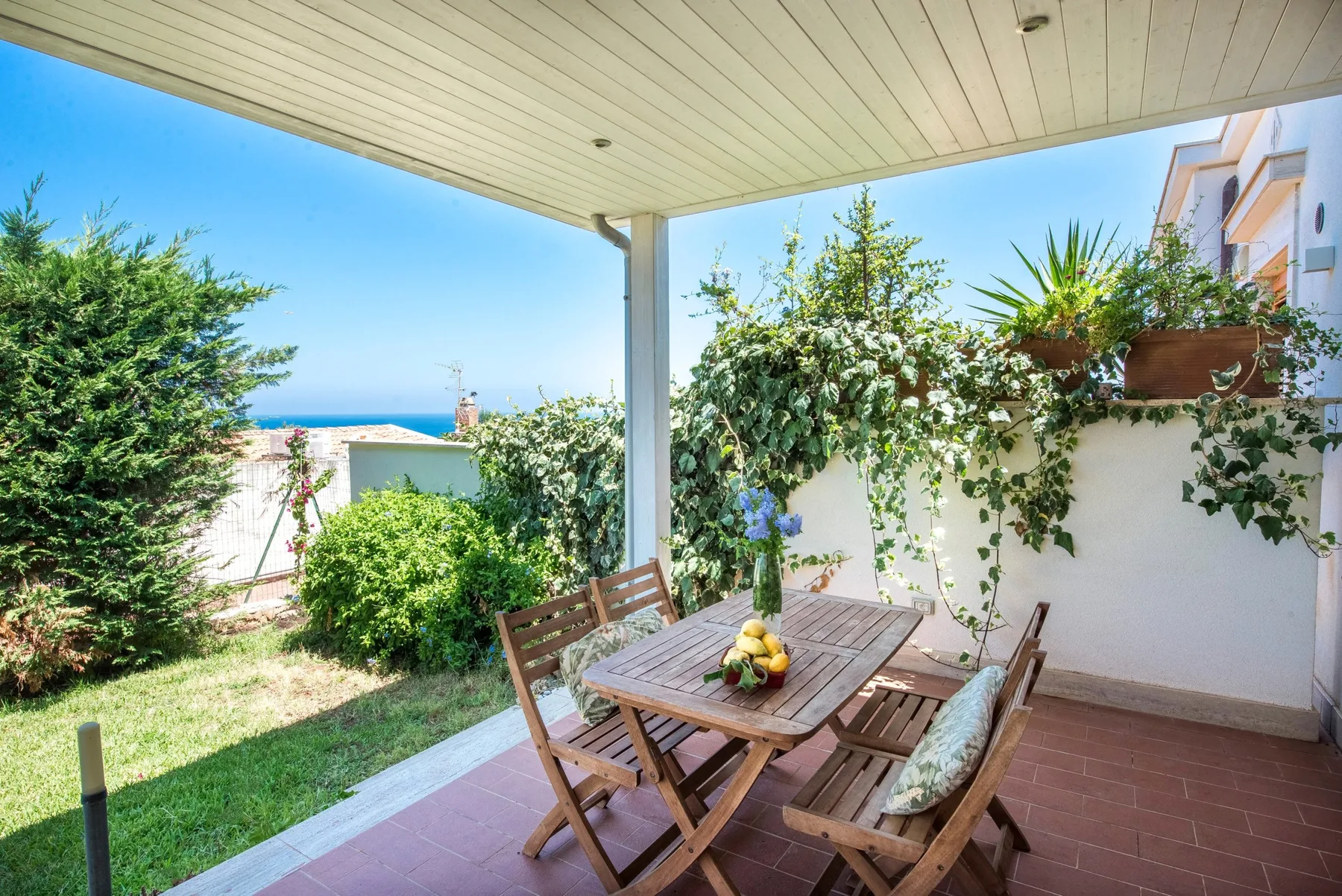 A covered outdoor patio with a wooden dining table and leafy garden views.