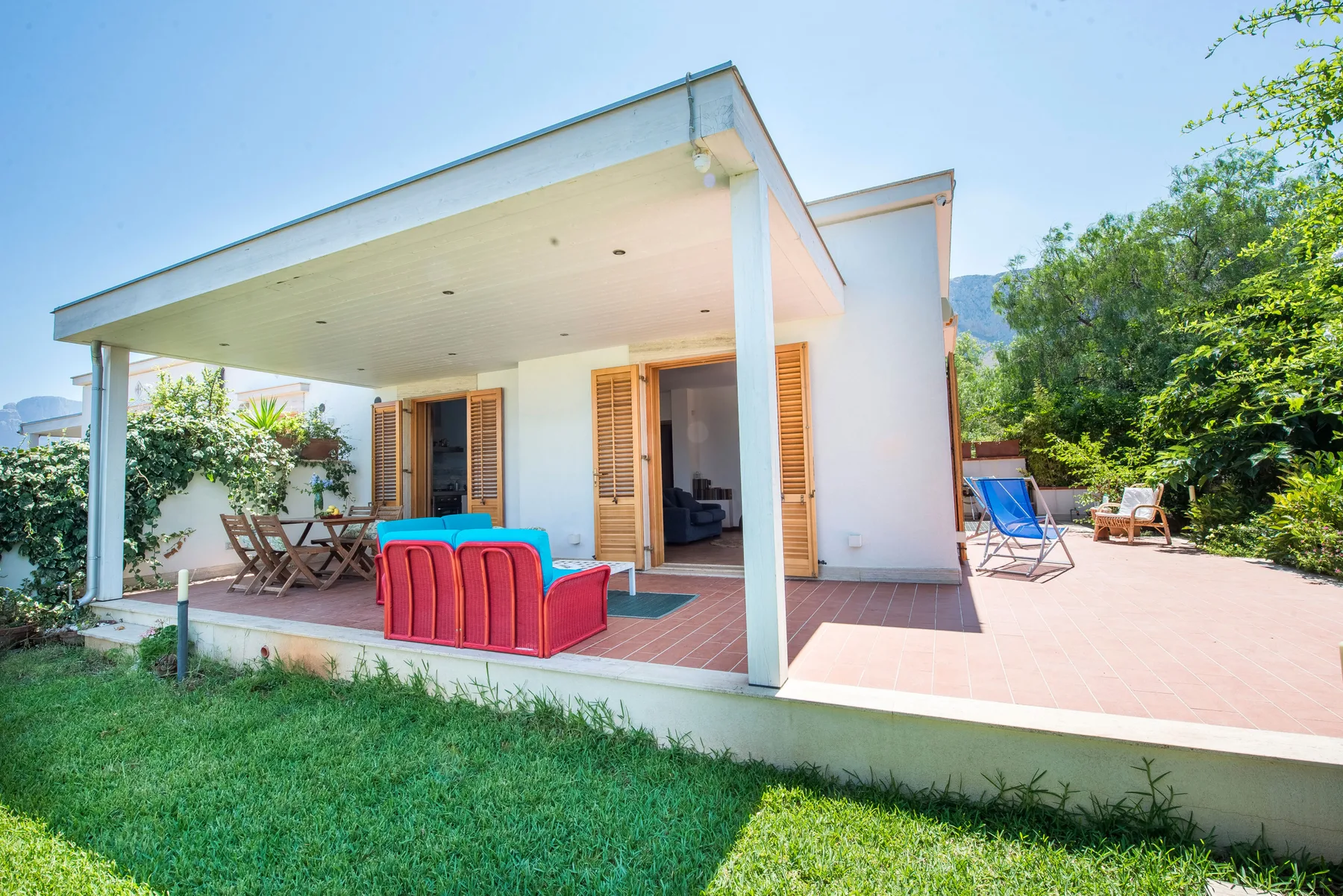 A modern house opens onto a covered patio with outdoor seating and a sunny terrace.