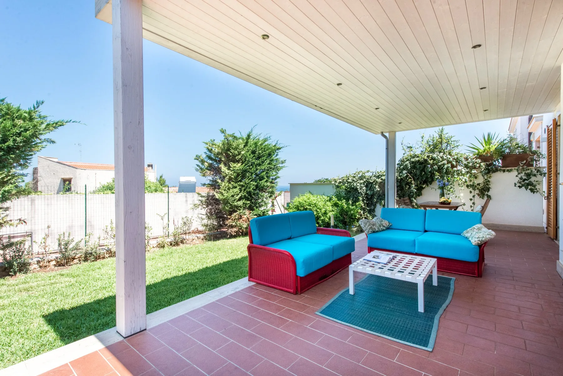 A covered outdoor patio has turquoise seating around a low table.