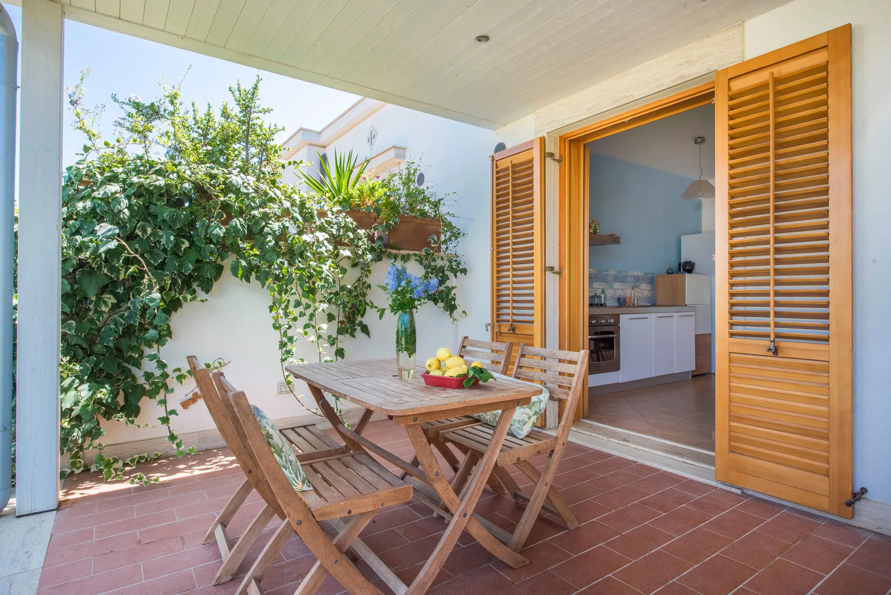 A patio dining area with wooden seating and an open doorway to a kitchen.