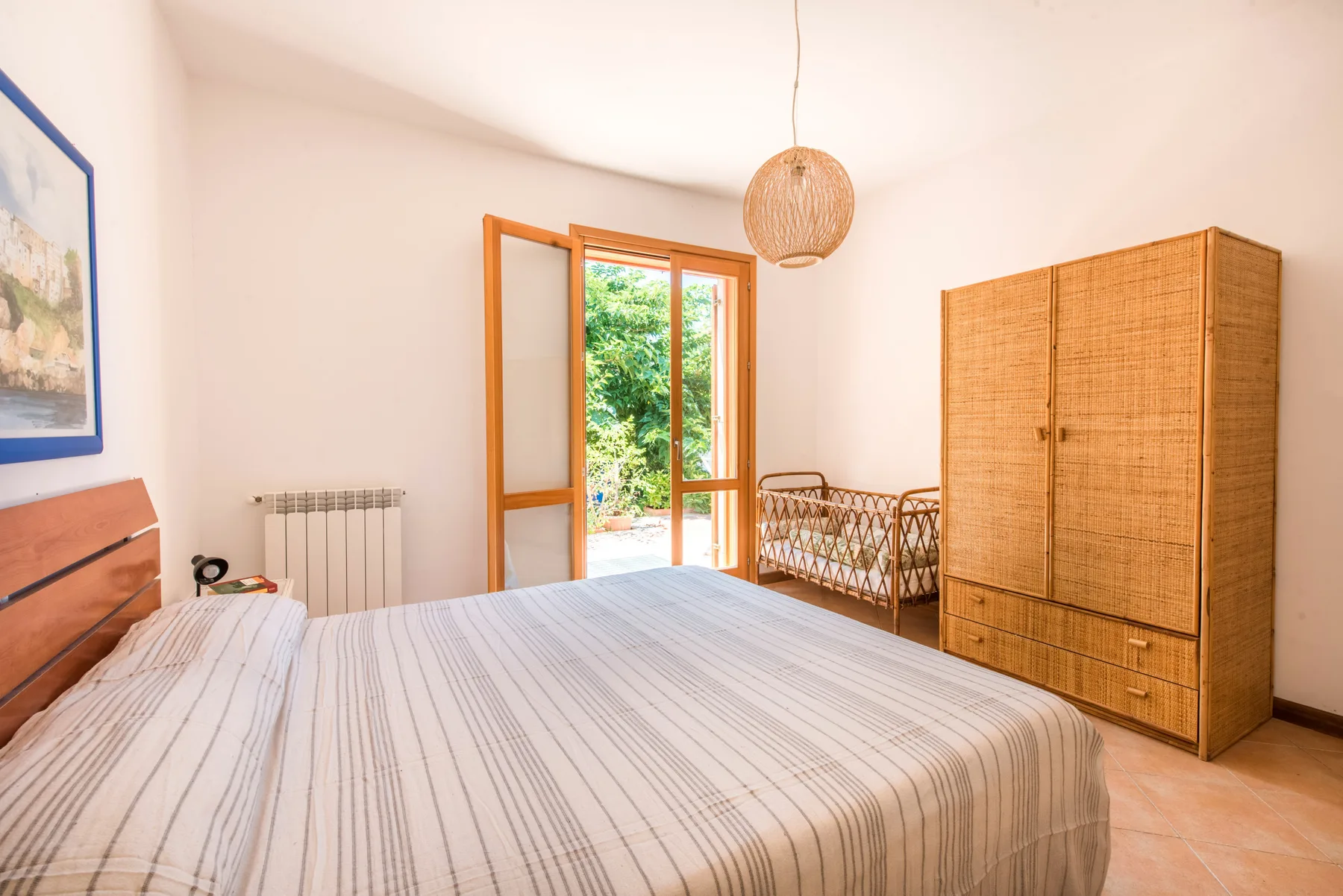 A bright bedroom with a large bed and a woven wardrobe.