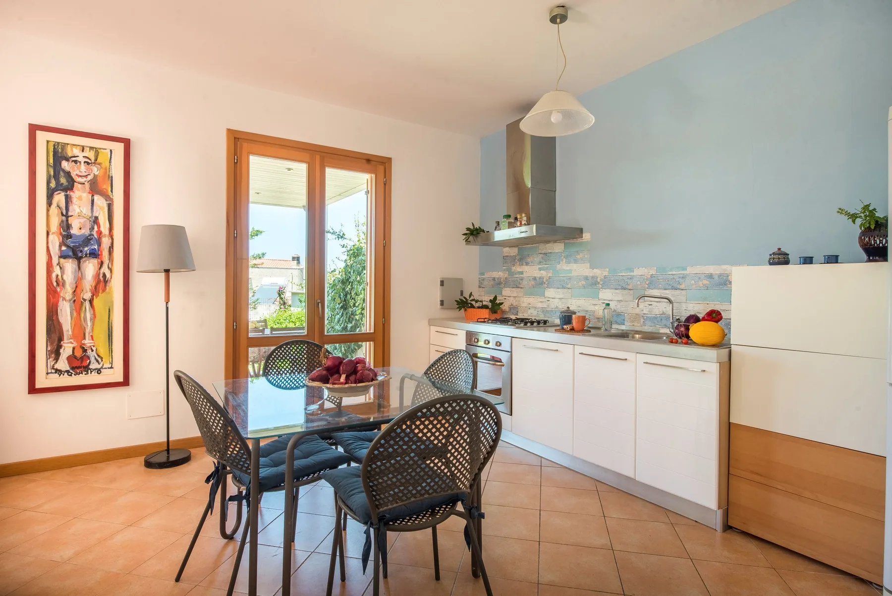 A bright kitchen and dining area with a glass table and blue accent wall.