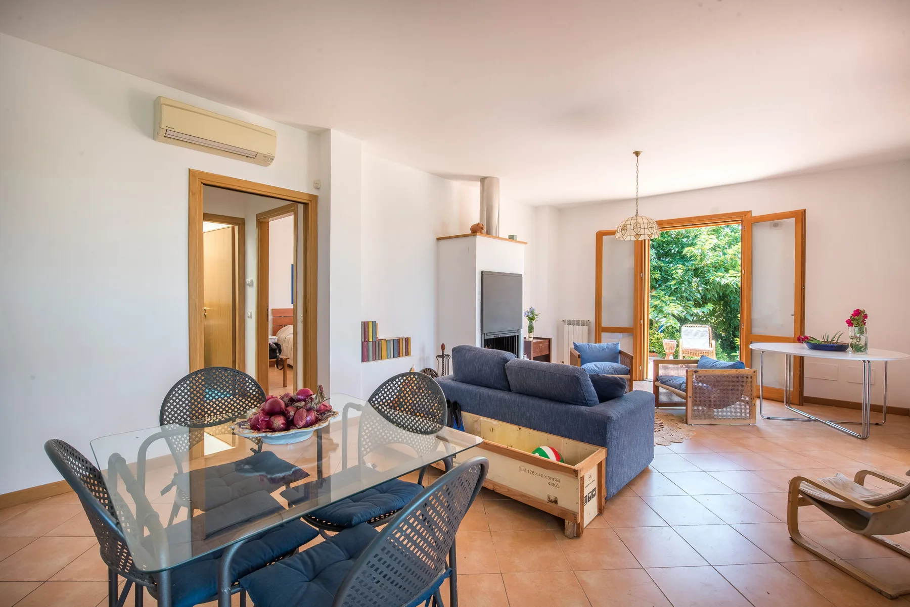 Living room with seating, a glass dining table, and open doors to greenery.