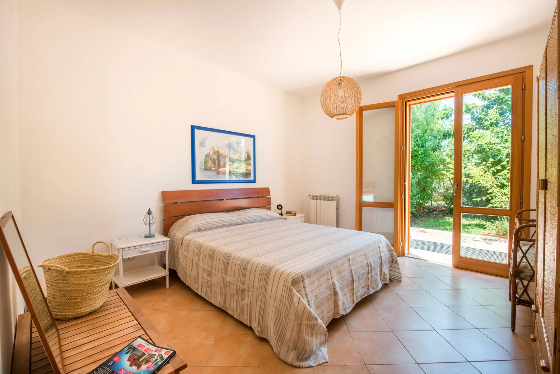 A bright bedroom with a bed beside open glass doors overlooking greenery.