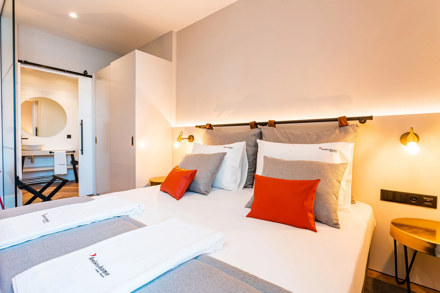 A bedroom with a neatly made bed and bright orange accent pillows.