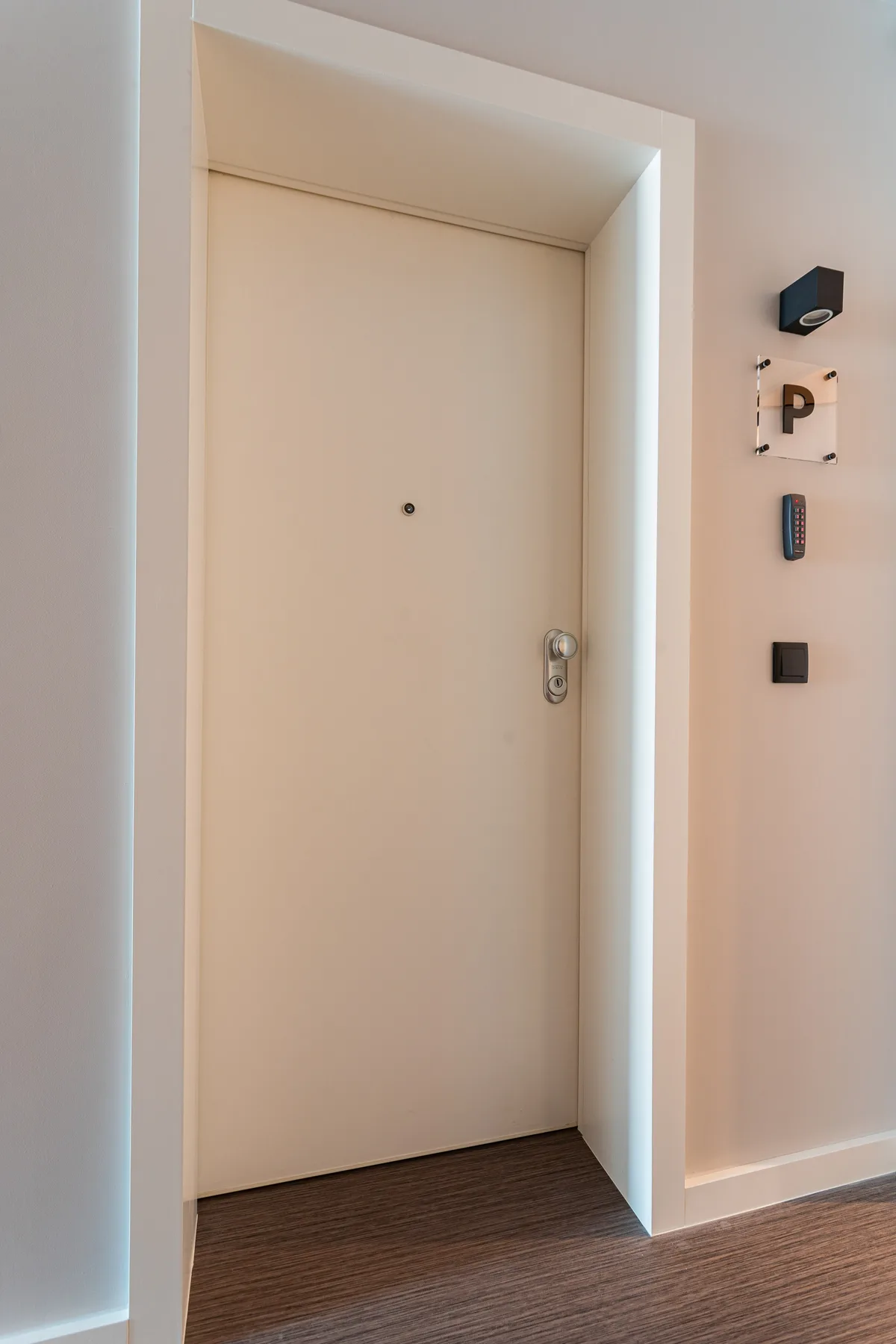 A beige entry door opens onto a hallway with wood flooring.