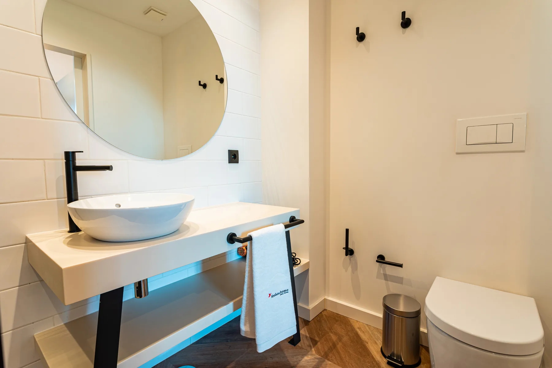 A bathroom with a vessel sink, round mirror, and toilet.