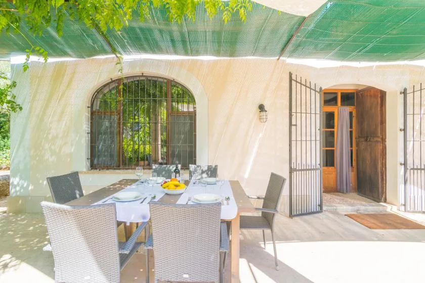 Comedor exterior a la sombra, con una mesa puesta junto a una puerta abierta.