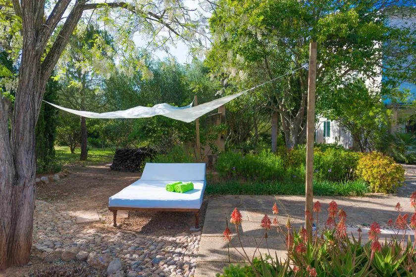Una zona de descanso sombreada en el jardín tiene una tumbona blanca bajo una vela de sombra.