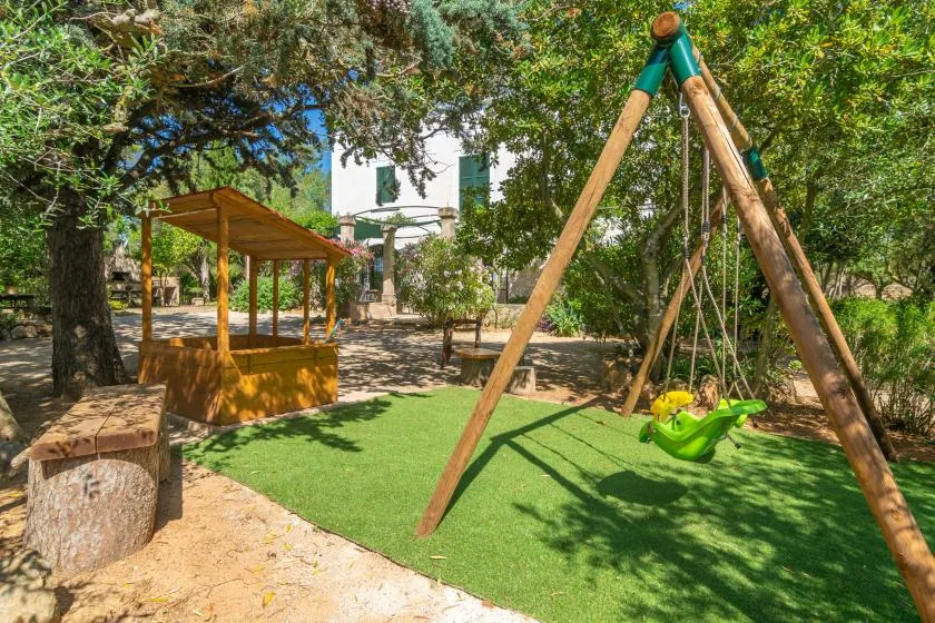 Una zona de juegos al aire libre con sombra, un columpio de madera y una pequeña estructura de juego.