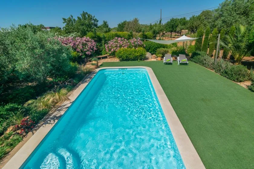 Una piscina al aire libre junto a un césped verde y un jardín.