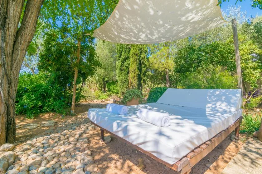 Una cama de exterior está bajo un toldo de sombra en un jardín frondoso.
