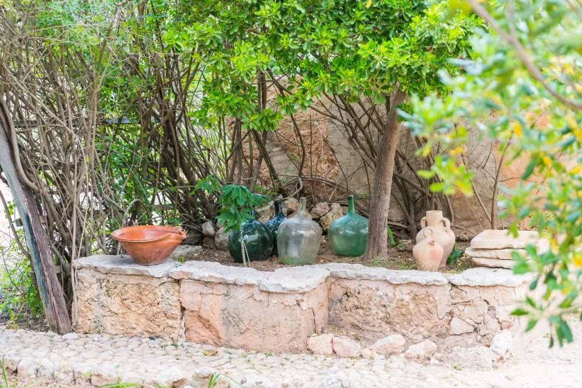 Un muro de piedra en un jardín exhibe varias vasijas de cerámica bajo árboles frondosos.
