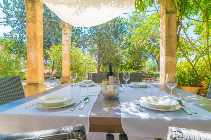 Una mesa de comedor al aire libre está preparada bajo un toldo, rodeada de vistas al jardín.