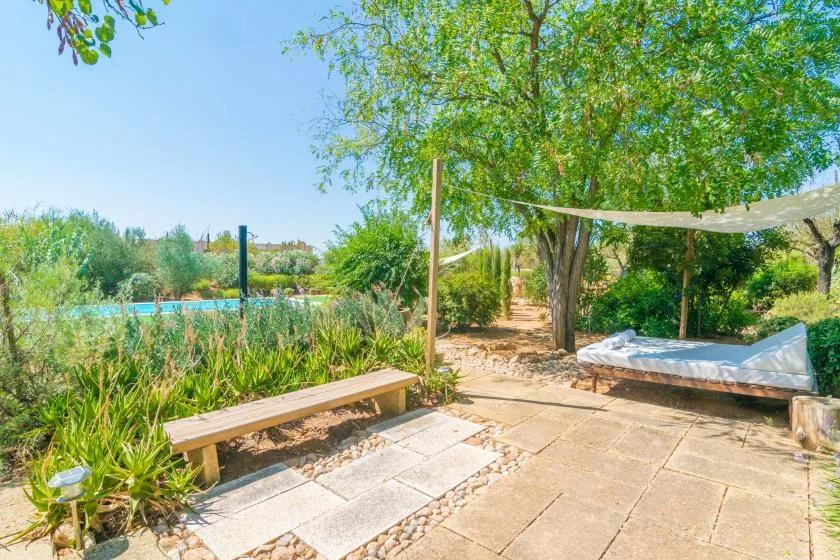 Un patio de jardín con sombra y un banco de madera junto a una piscina.