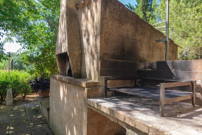 Una zona de estar al aire libre junto a una gran chimenea de mampostería, rodeada de árboles.