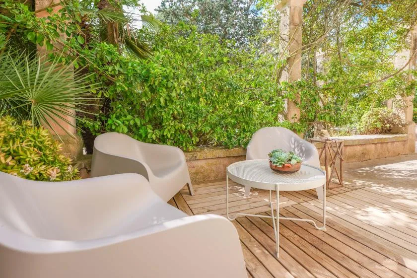 Un patio ajardinado con asientos exteriores y una mesa pequeña entre abundante vegetación.