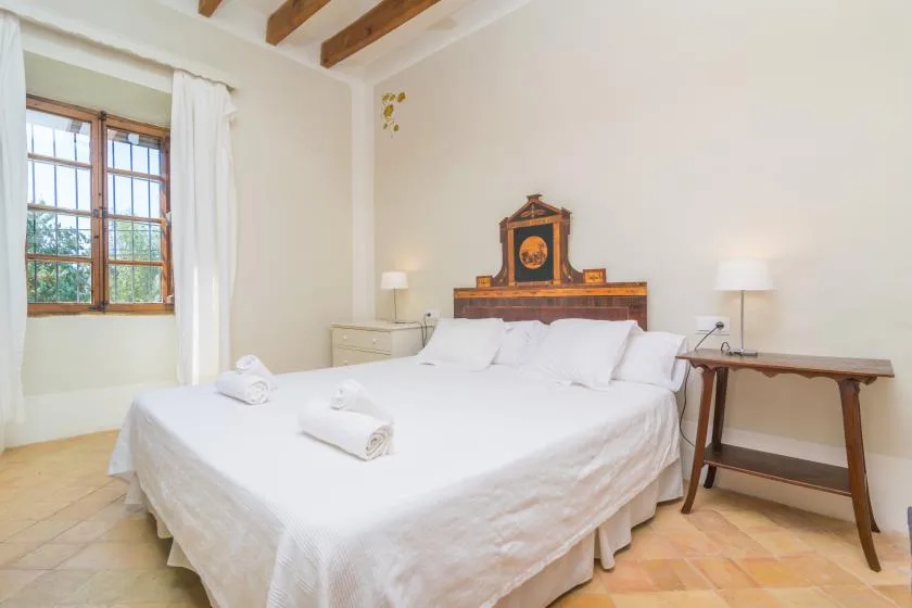 Un dormitorio luminoso con una cama grande, cabecero de madera y una ventana.
