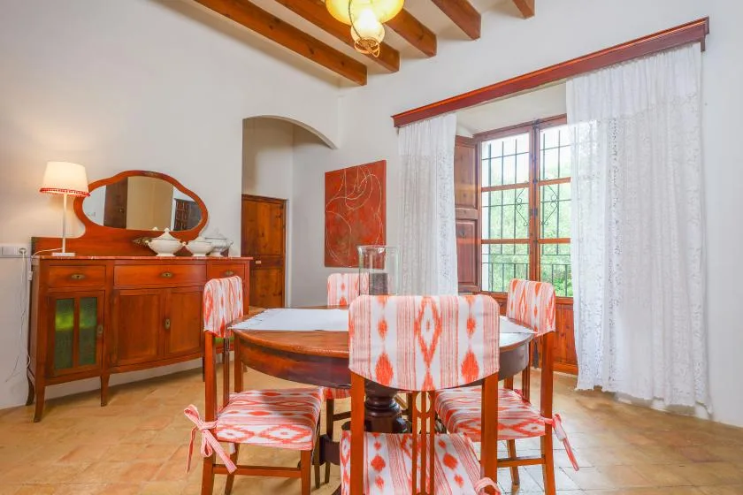 Un comedor con una mesa y sillas de madera junto a una gran ventana con cortinas.