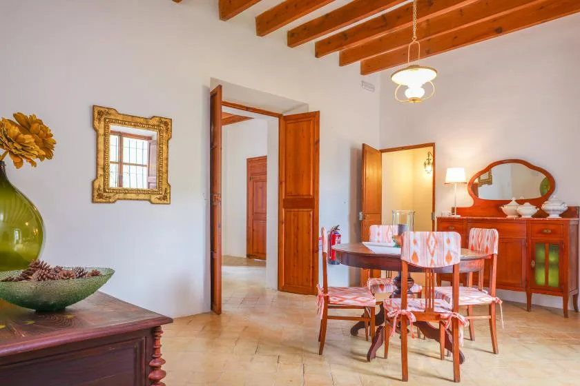 Un comedor con una mesa y sillas de madera está bajo vigas de techo expuestas.