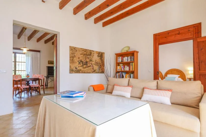 Una sala de estar con asientos beige, una mesa de centro de vidrio y vigas de madera expuestas.