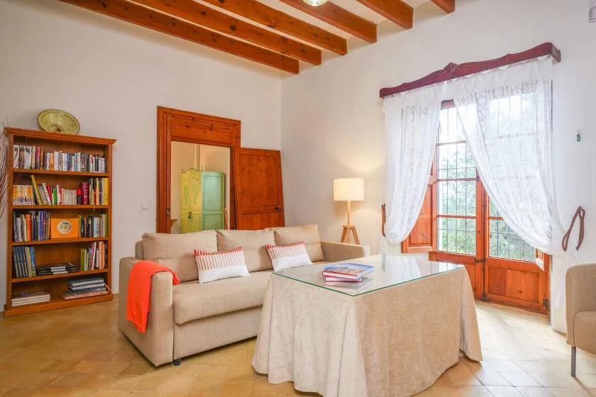 Una sala de estar con un sofá beige, una mesa cubierta y una ventana luminosa.