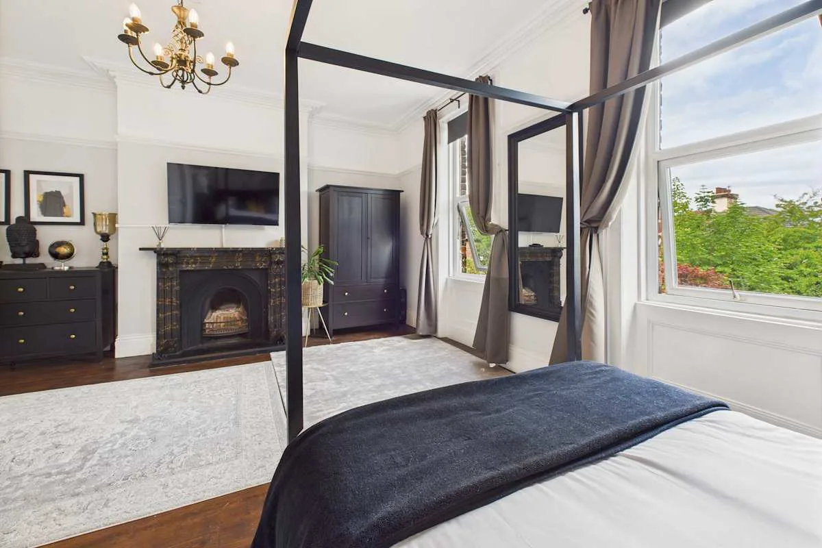 Un dormitorio con cama con dosel, chimenea y ventanas grandes.
