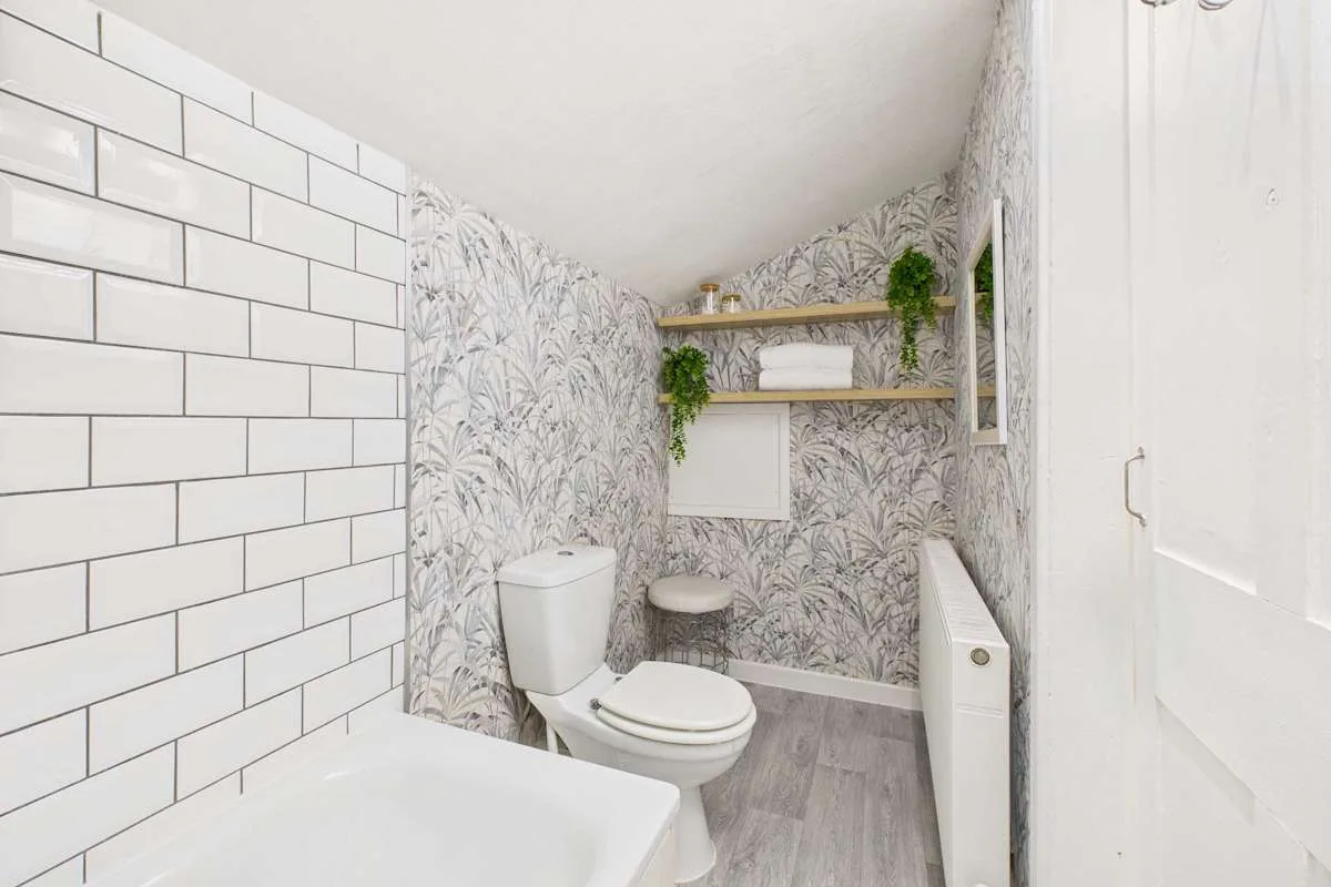 Un baño con inodoro, lavabo y paredes con estampado de hojas.