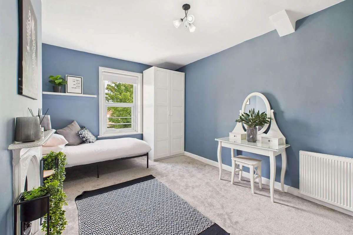 Un dormitorio azul con una cama, un tocador pequeño y una ventana.