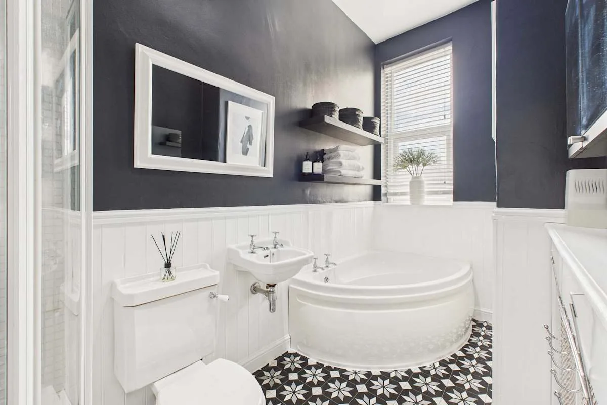 Un baño con bañera, lavabo con pedestal y suelo de baldosas estampadas.