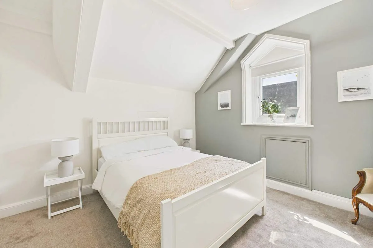 Un dormitorio luminoso con una cama bajo un techo inclinado y una ventana.