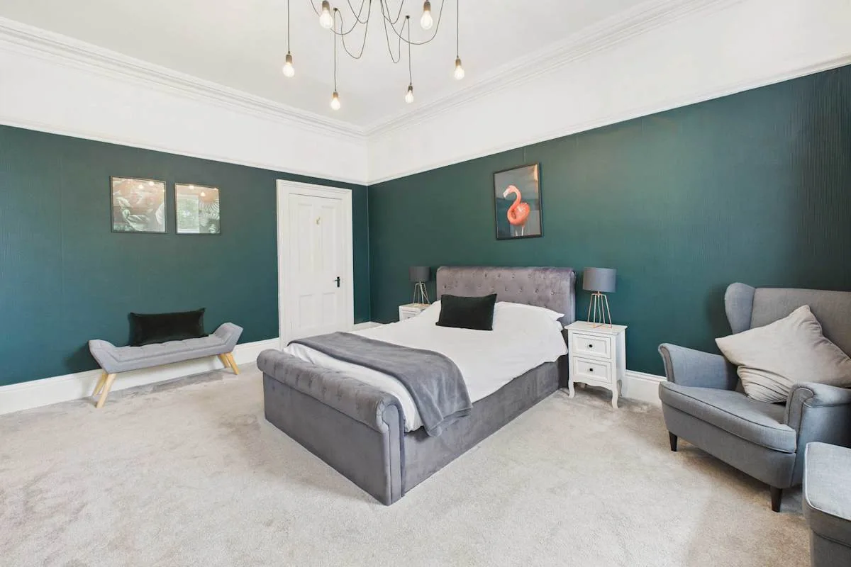 Un dormitorio con una cama grande, paredes verde oscuro y un sillón.