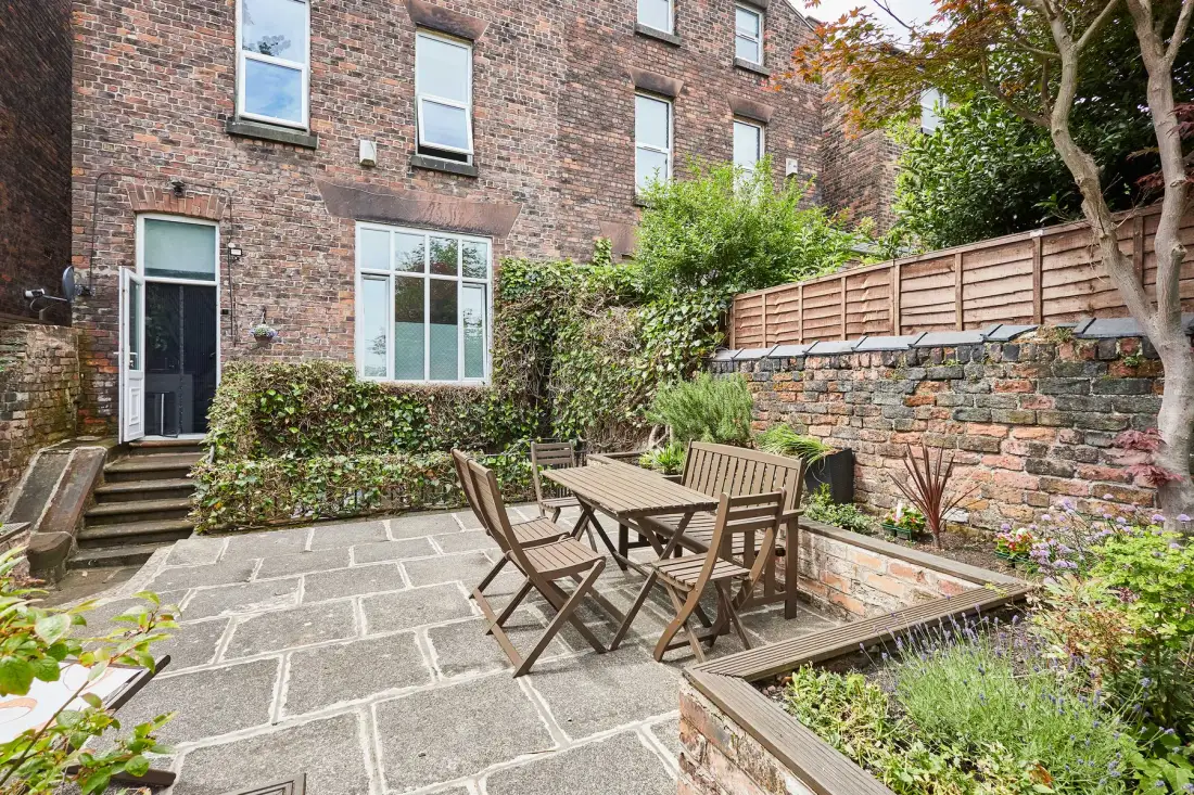 Un patio ajardinado pavimentado con asientos al aire libre y jardineras elevadas.