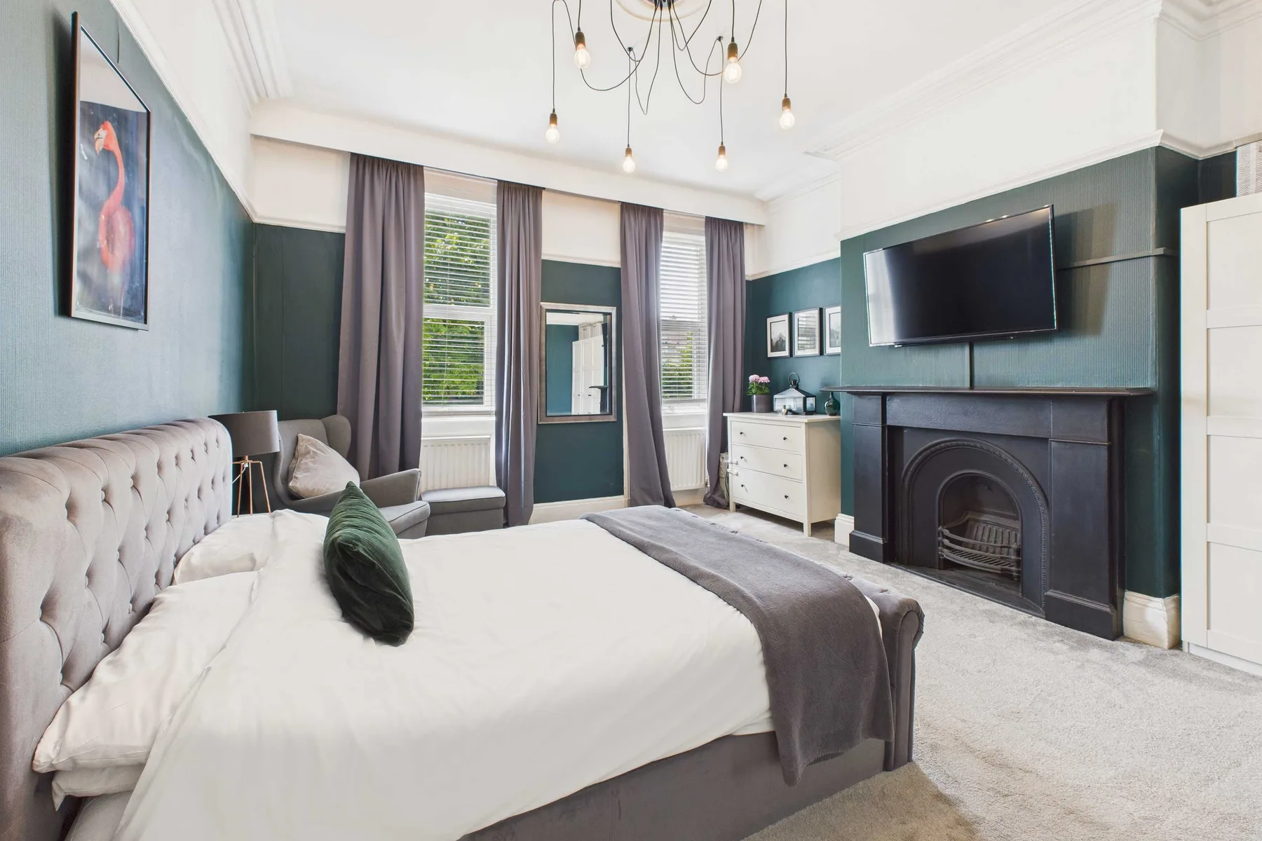 Un dormitorio luminoso con una cama grande, ventanas con cortinas y una chimenea.