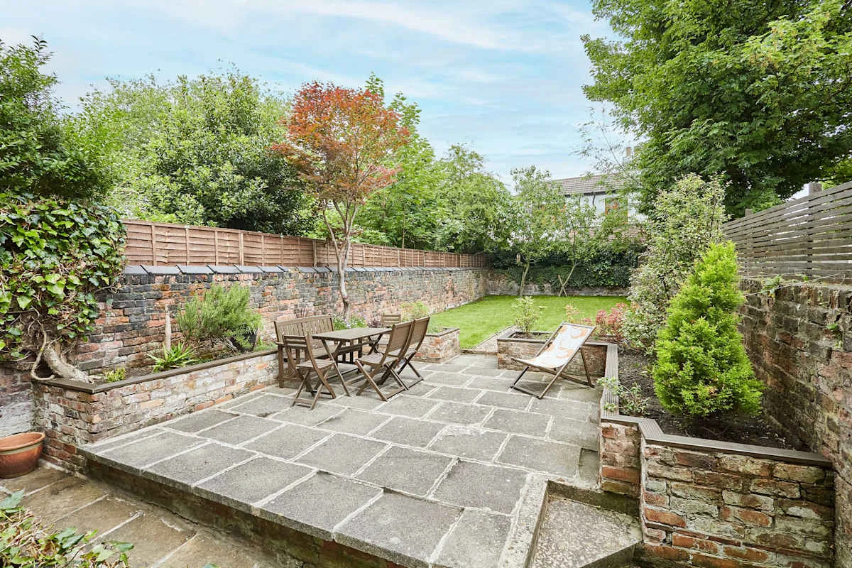 Un patio de jardín pavimentado tiene asientos al aire libre y jardineras elevadas.