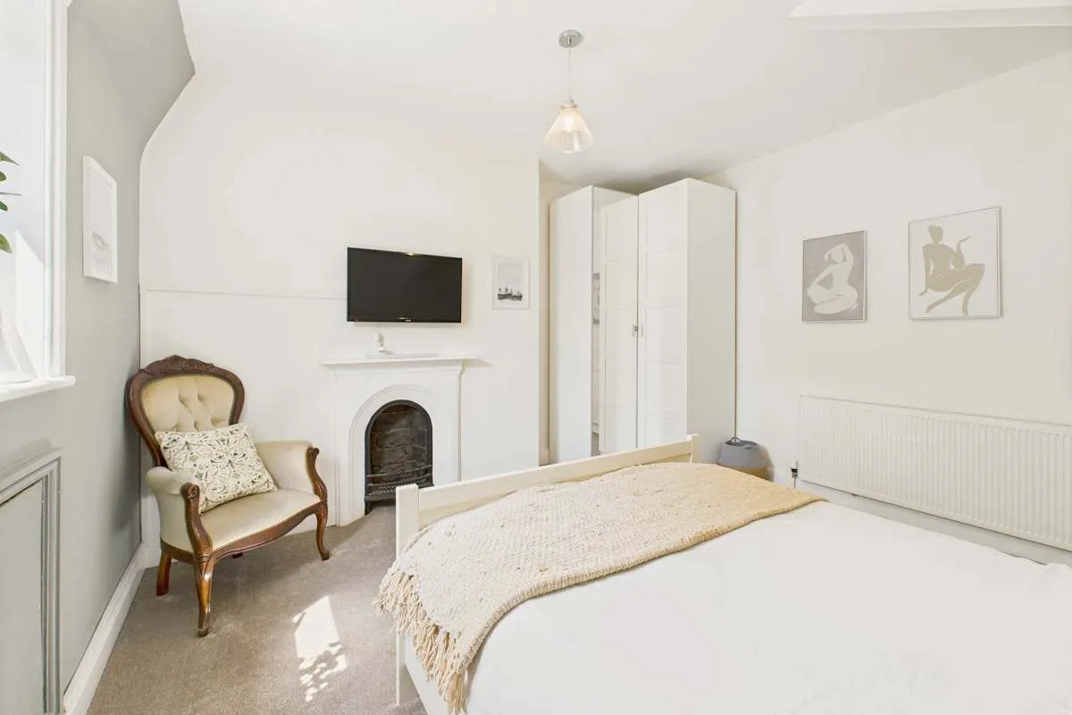 Un dormitorio luminoso con una cama, un sillón y un televisor sobre la chimenea.