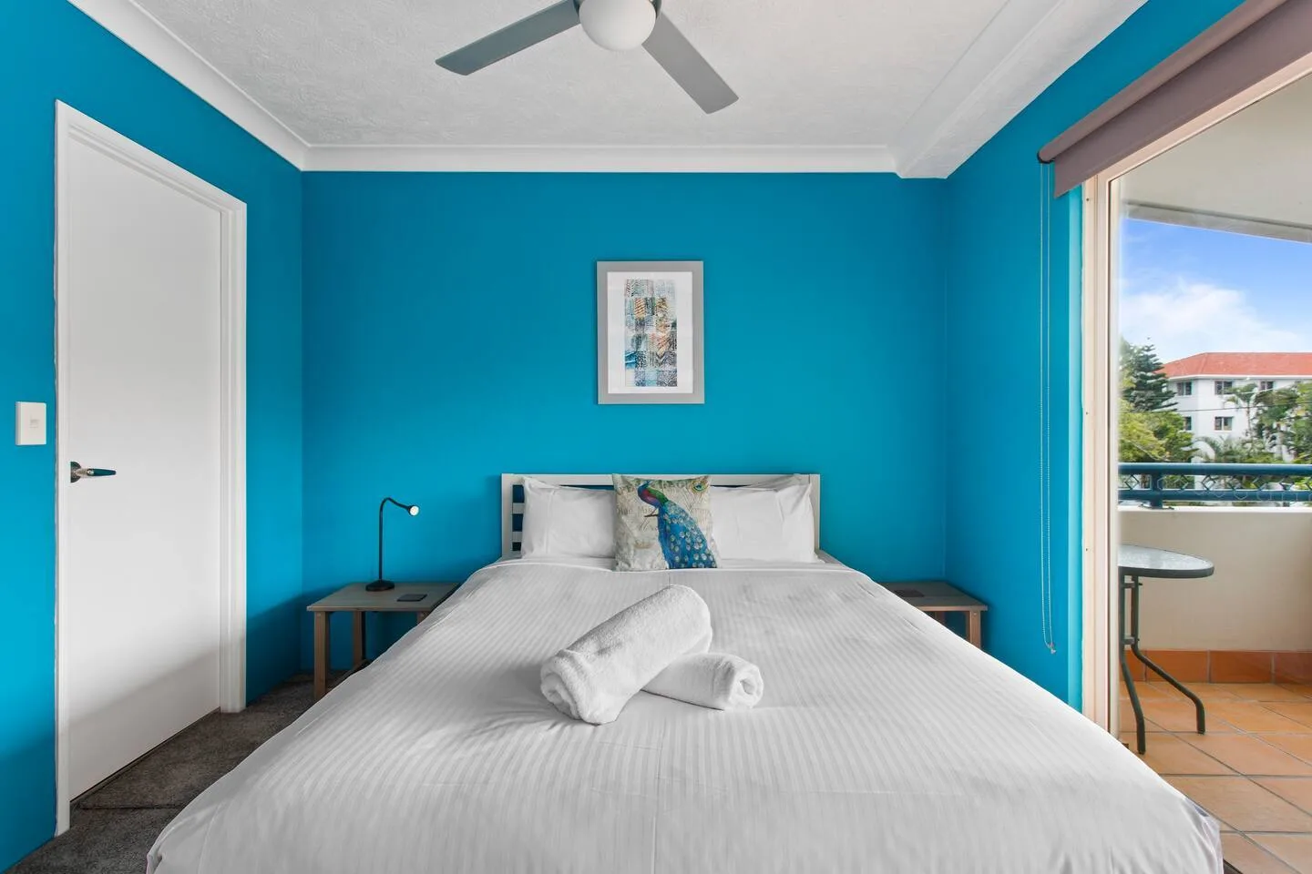A bedroom with a double bed, bedside tables, and an open sliding glass door.
