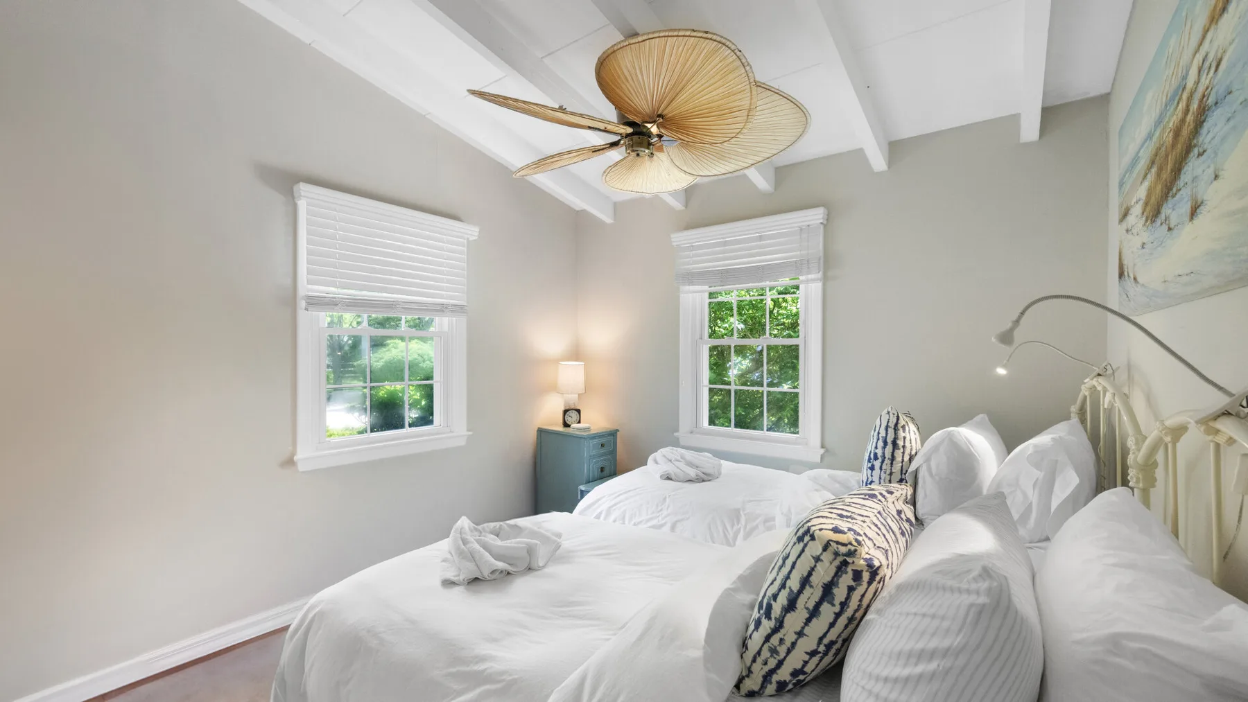 Un dormitorio luminoso con ropa de cama blanca, dos ventanas y un ventilador de techo.