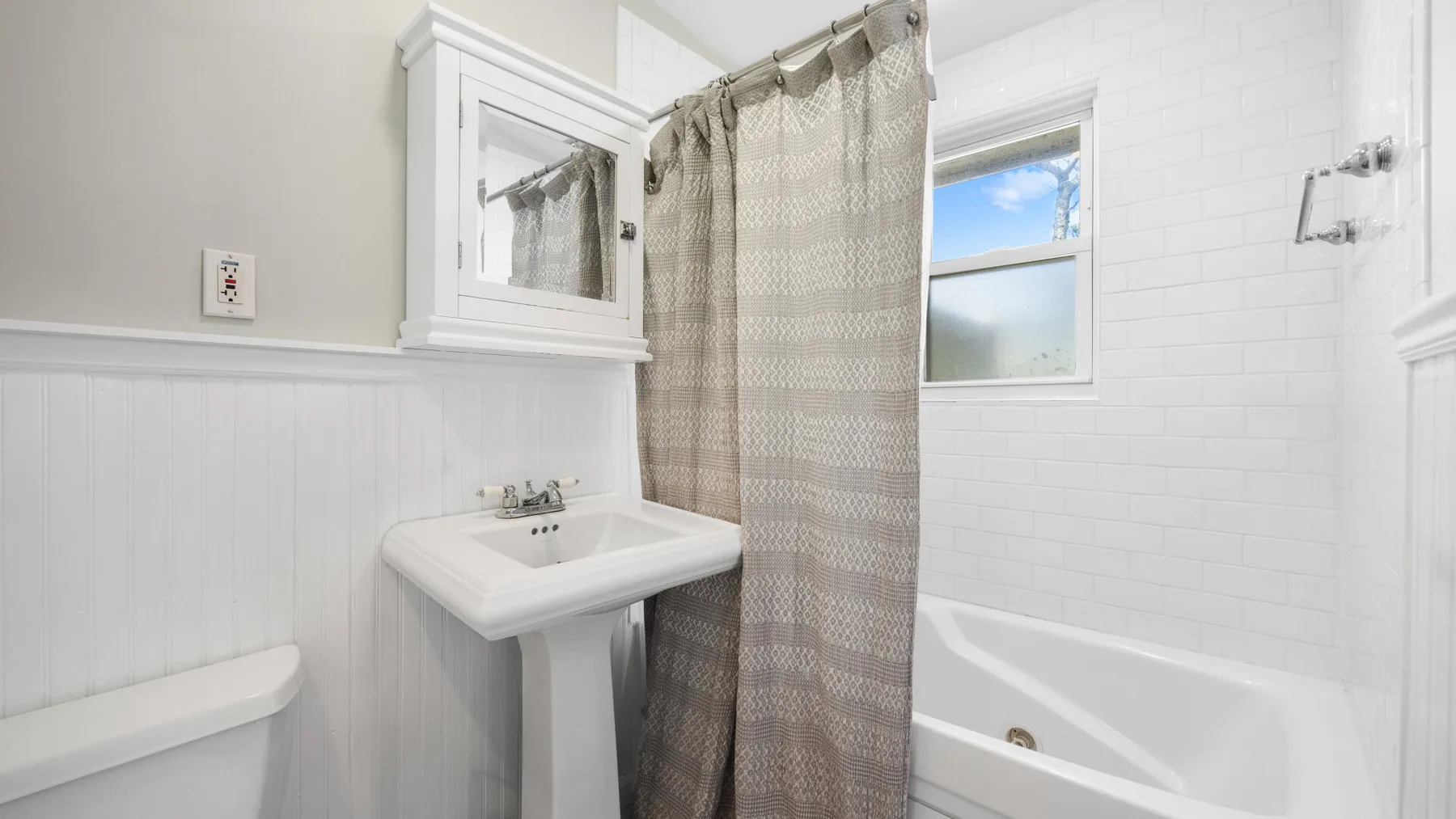 Un baño con lavabo de pedestal, bañera y cortina de ducha estampada.