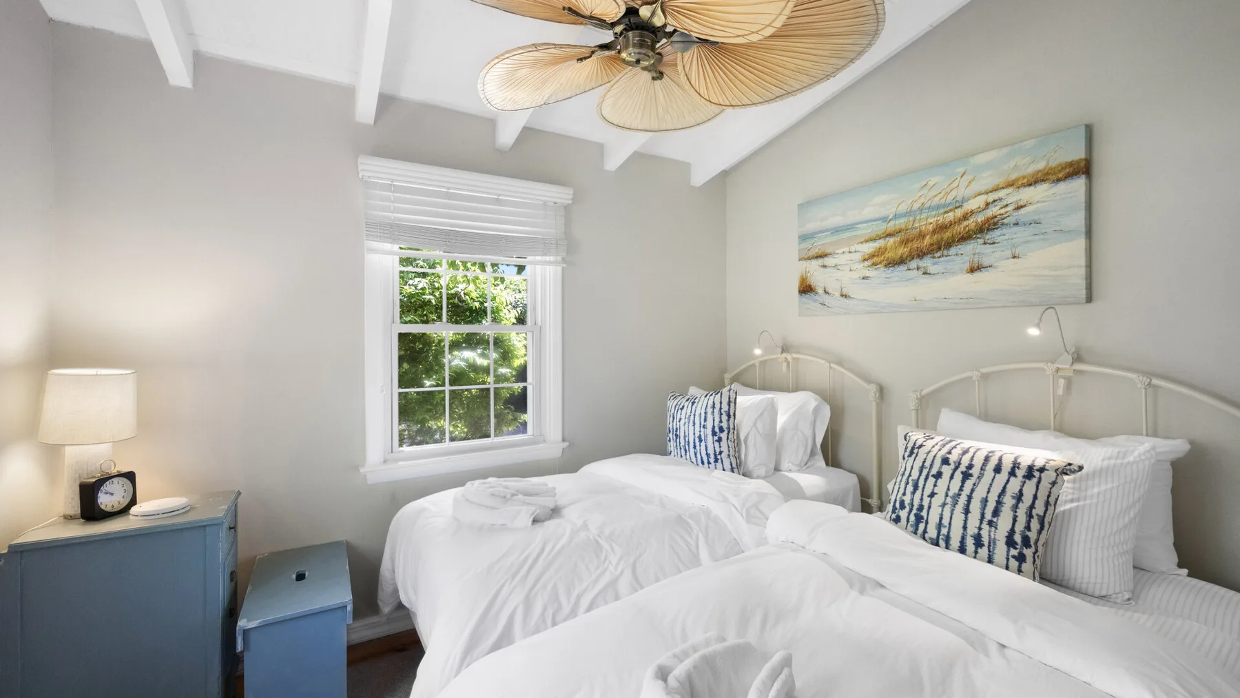 Un dormitorio luminoso con ropa de cama blanca, detalles azules y una ventana.