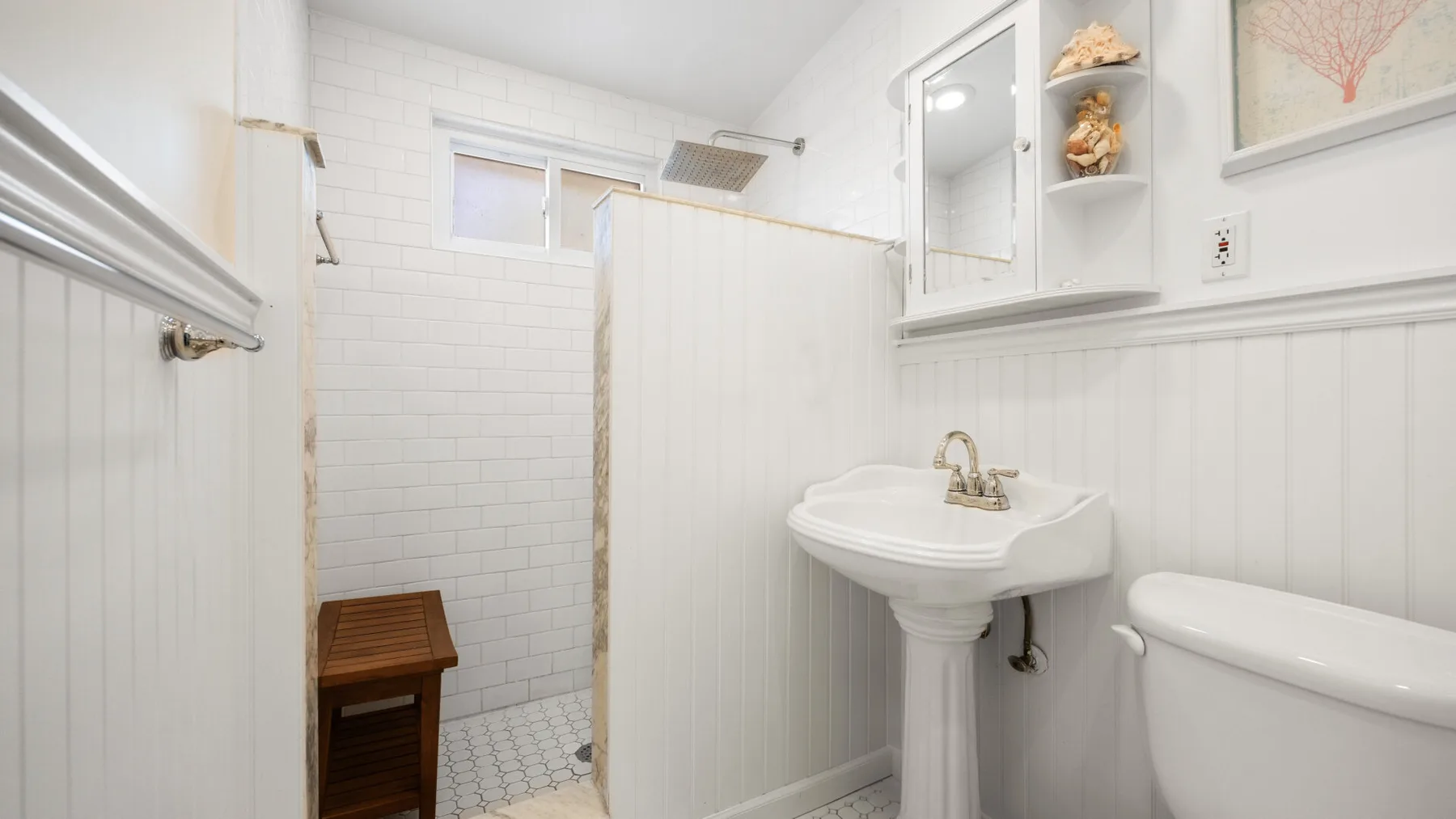 Un baño luminoso con lavabo de pedestal, inodoro y zona de ducha con azulejos.