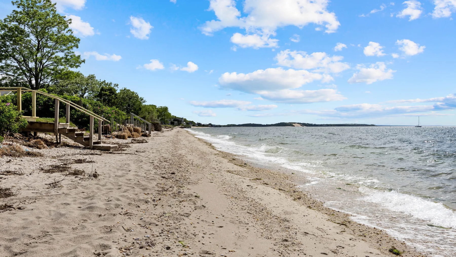 Una playa de arena bordea aguas tranquilas bajo un cielo parcialmente nublado.