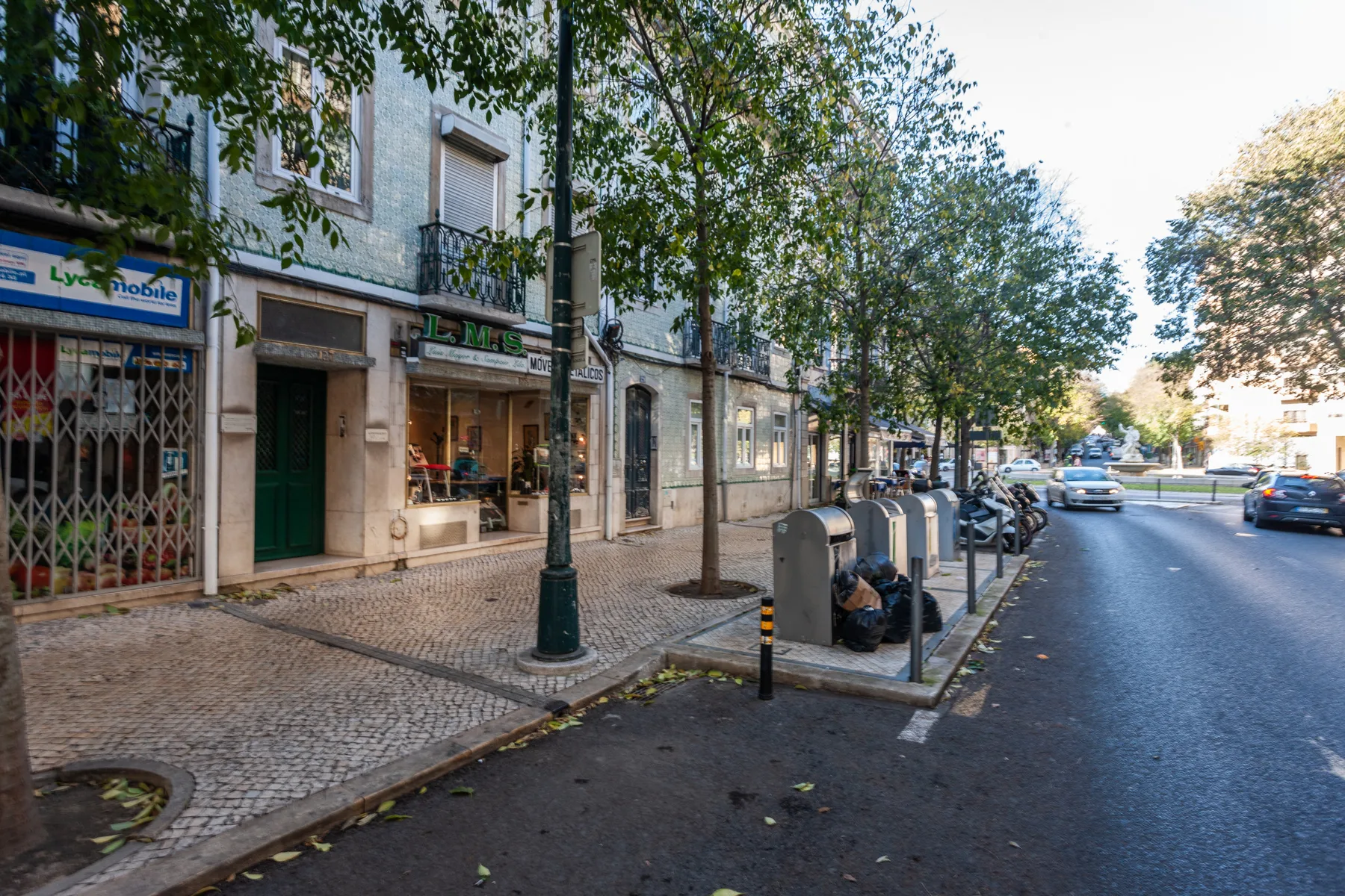 A city street lined with storefronts, trees, and parked cars.