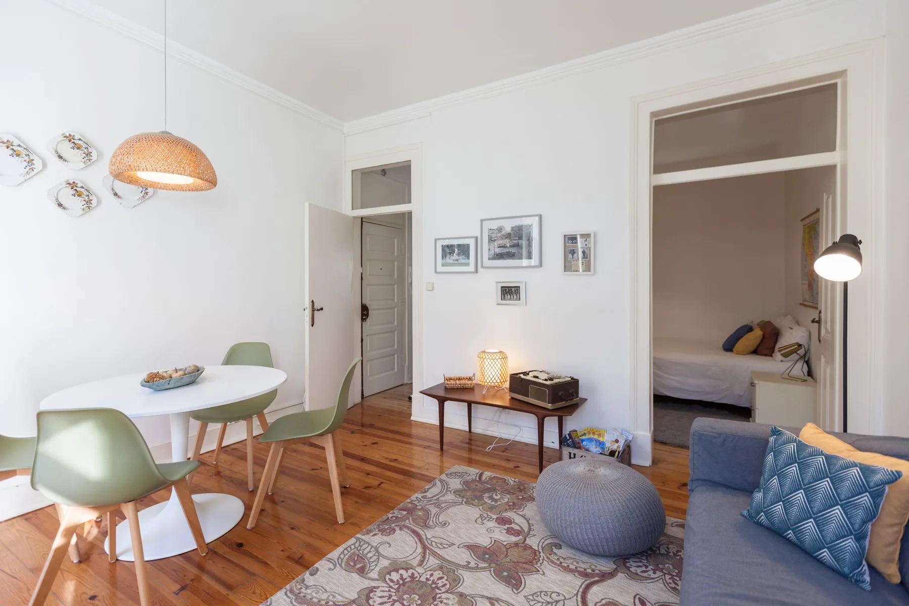 A bright living and dining area with seating, a table, and an open doorway to a bedroom.