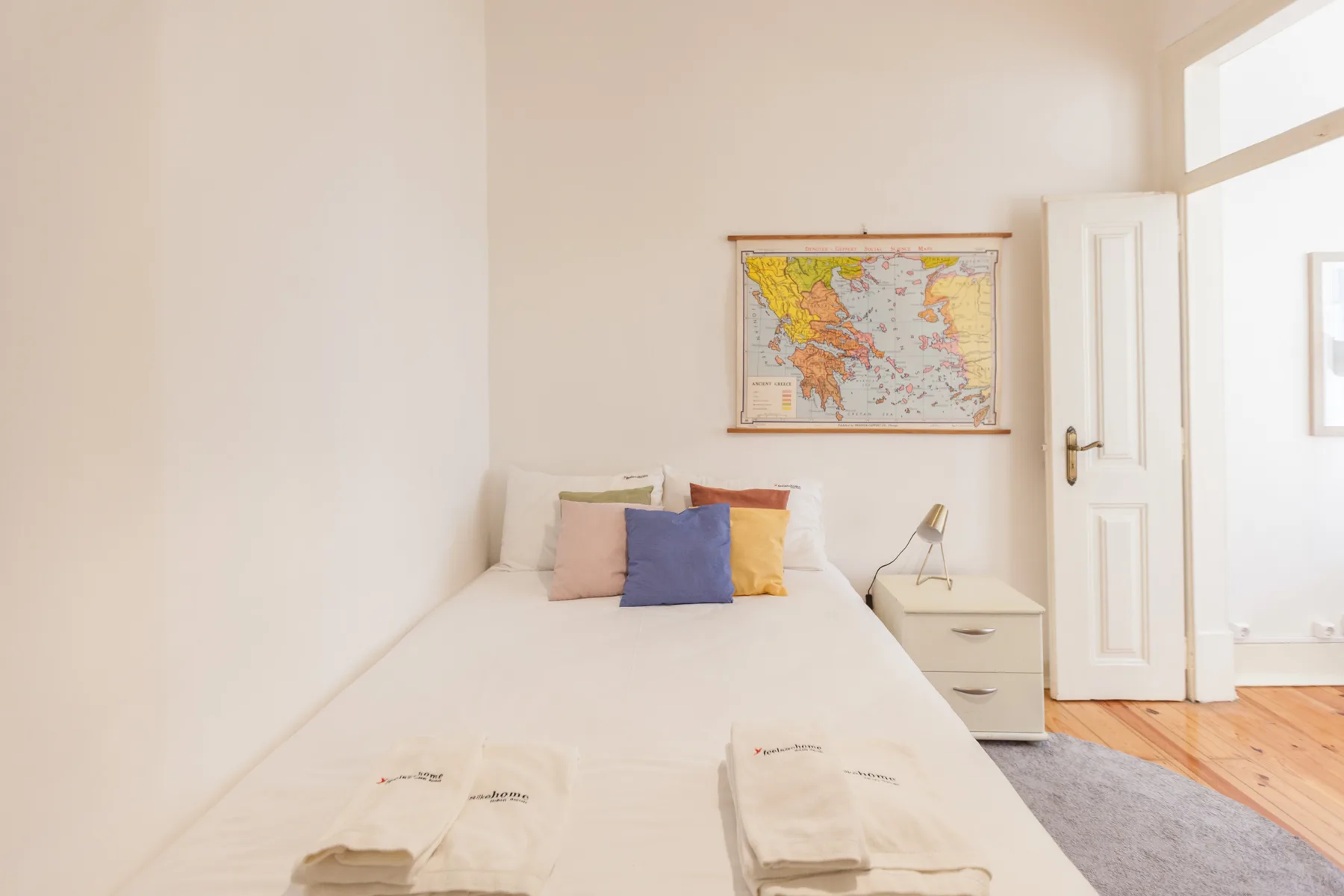 A bright bedroom with a neatly made bed and a colorful map on the wall.