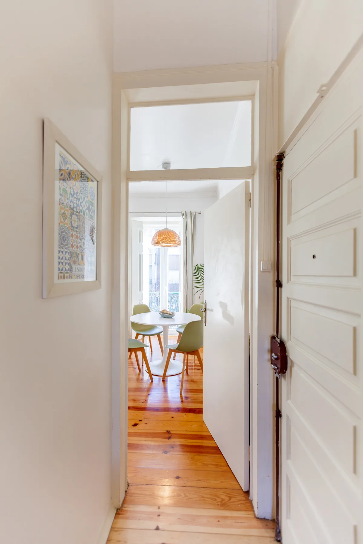 A bright apartment entryway opens onto a dining area with a wooden floor.