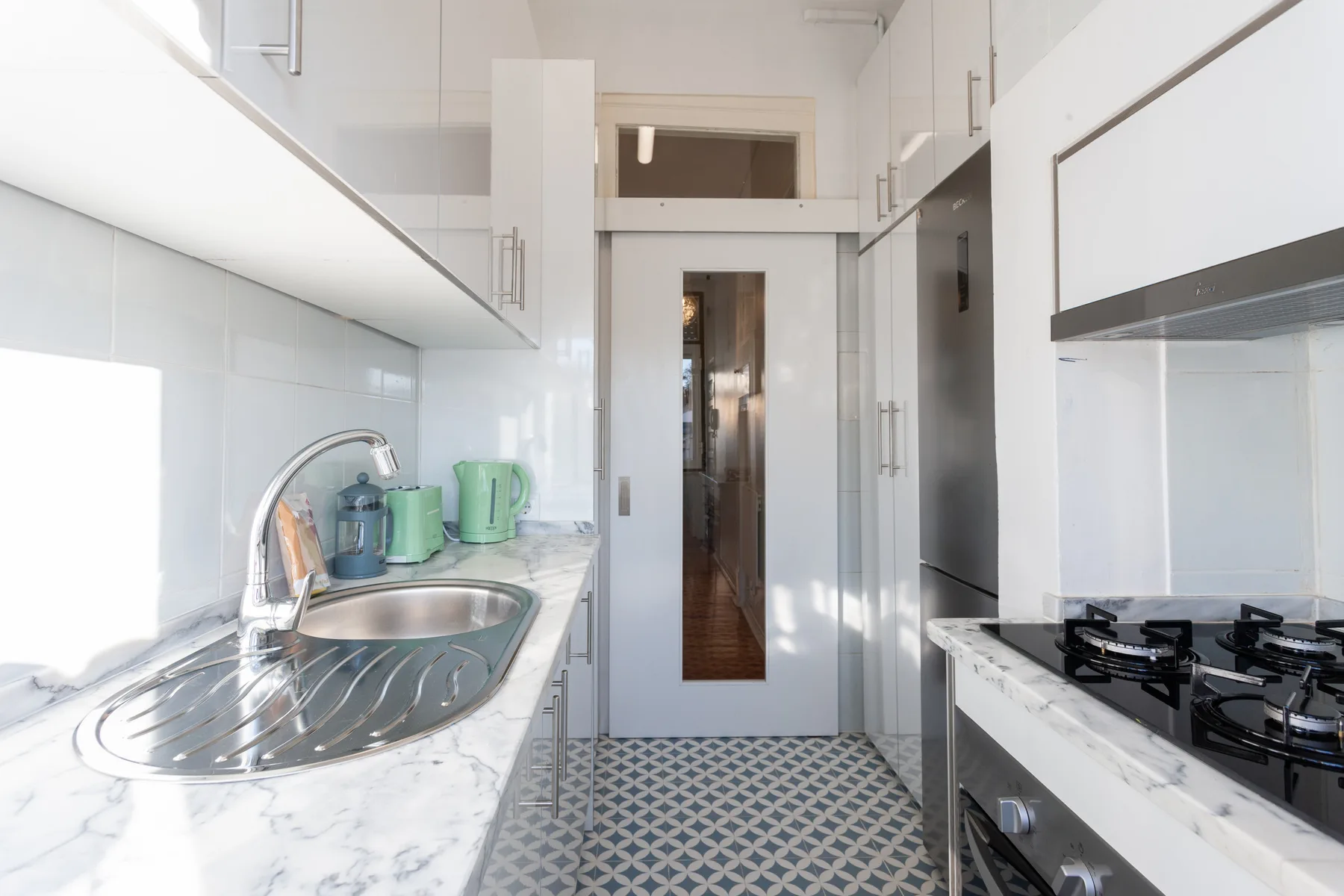A bright kitchen with white cabinetry, a sink, and a cooktop.