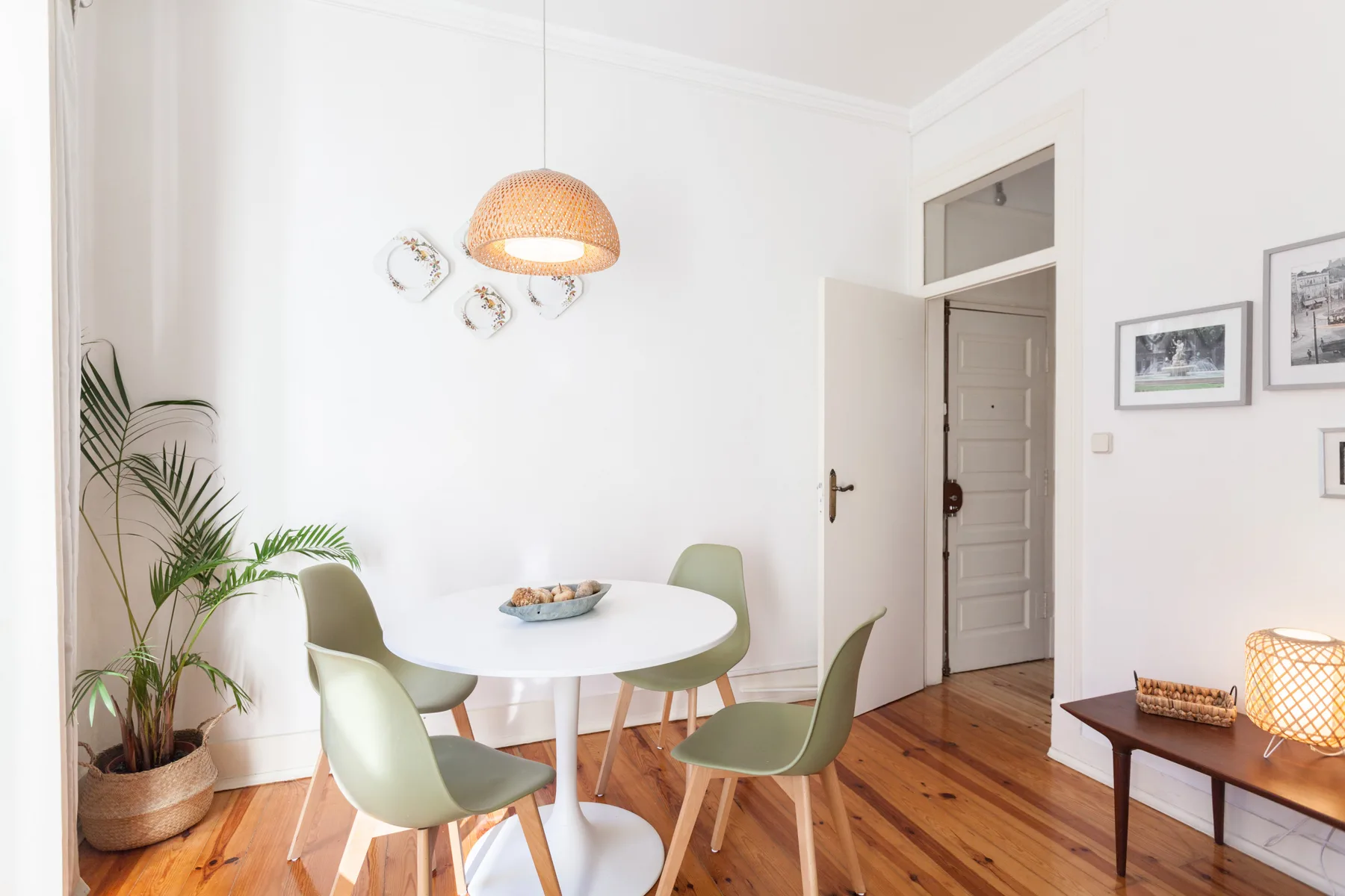 A bright dining area with a round table, green seating, and framed pictures.