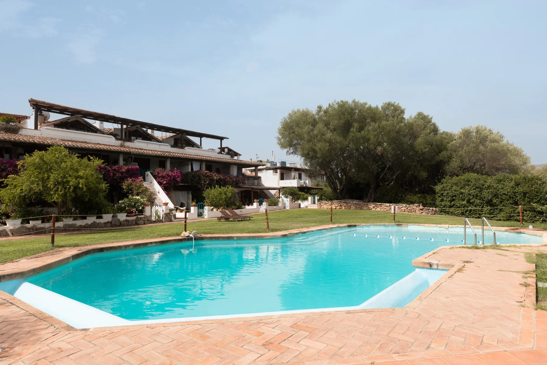 Una piscina al aire libre junto a un edificio ajardinado y un jardín.
