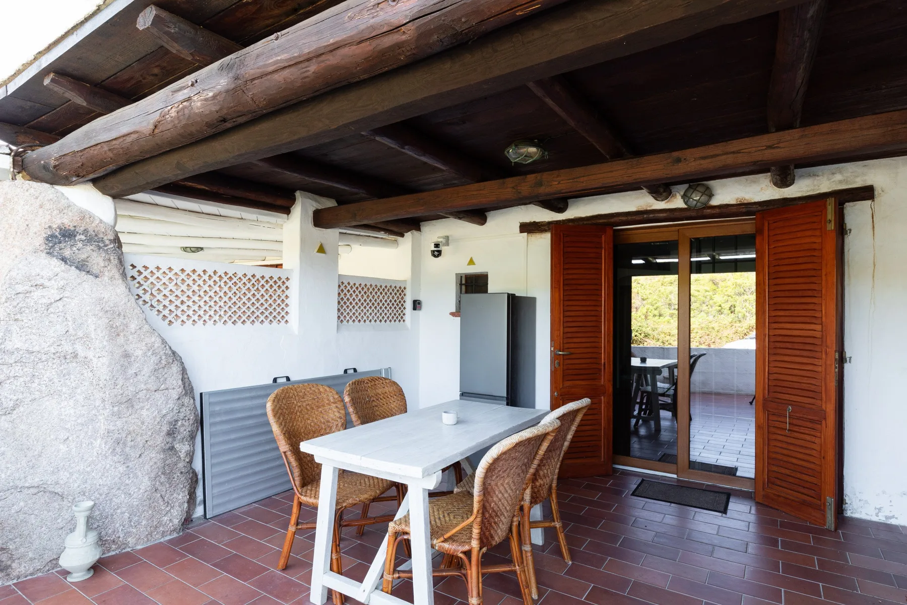 Un patio cubierto con una mesa y sillas junto a puertas de madera abiertas.